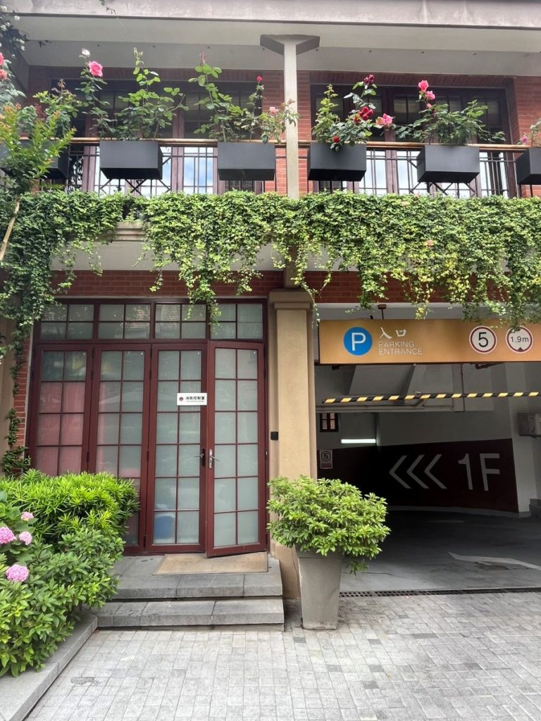 Balcon moderne avec jardinières de rosiers et lierre retombant au-dessus d’une entrée d’immeuble