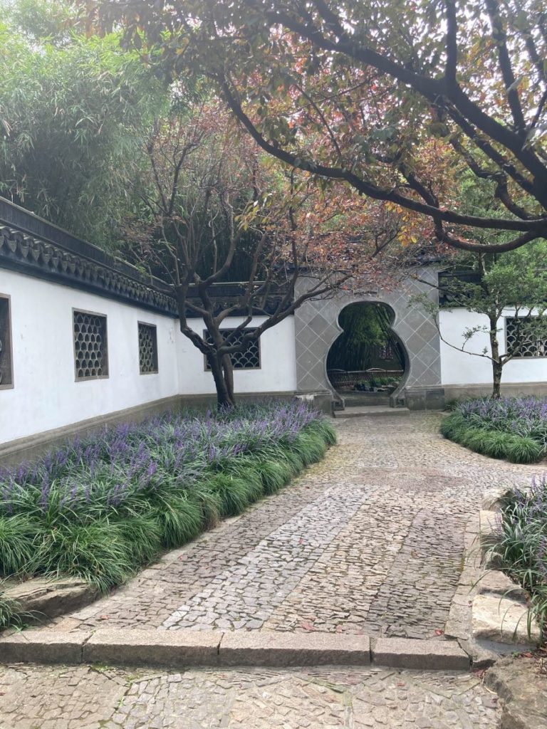 Photo montrant un jardin où des espaces sont délimités par des variations de pavés au sol, et deux niveaux avec des plantes et une architecture de jardin traditionnelle