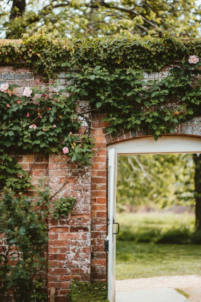 Une vieille porte ornée de roses grimpantes, s'ouvre sur un exterieur , invitant à la continuité entre le jardin clos et l'extérieur