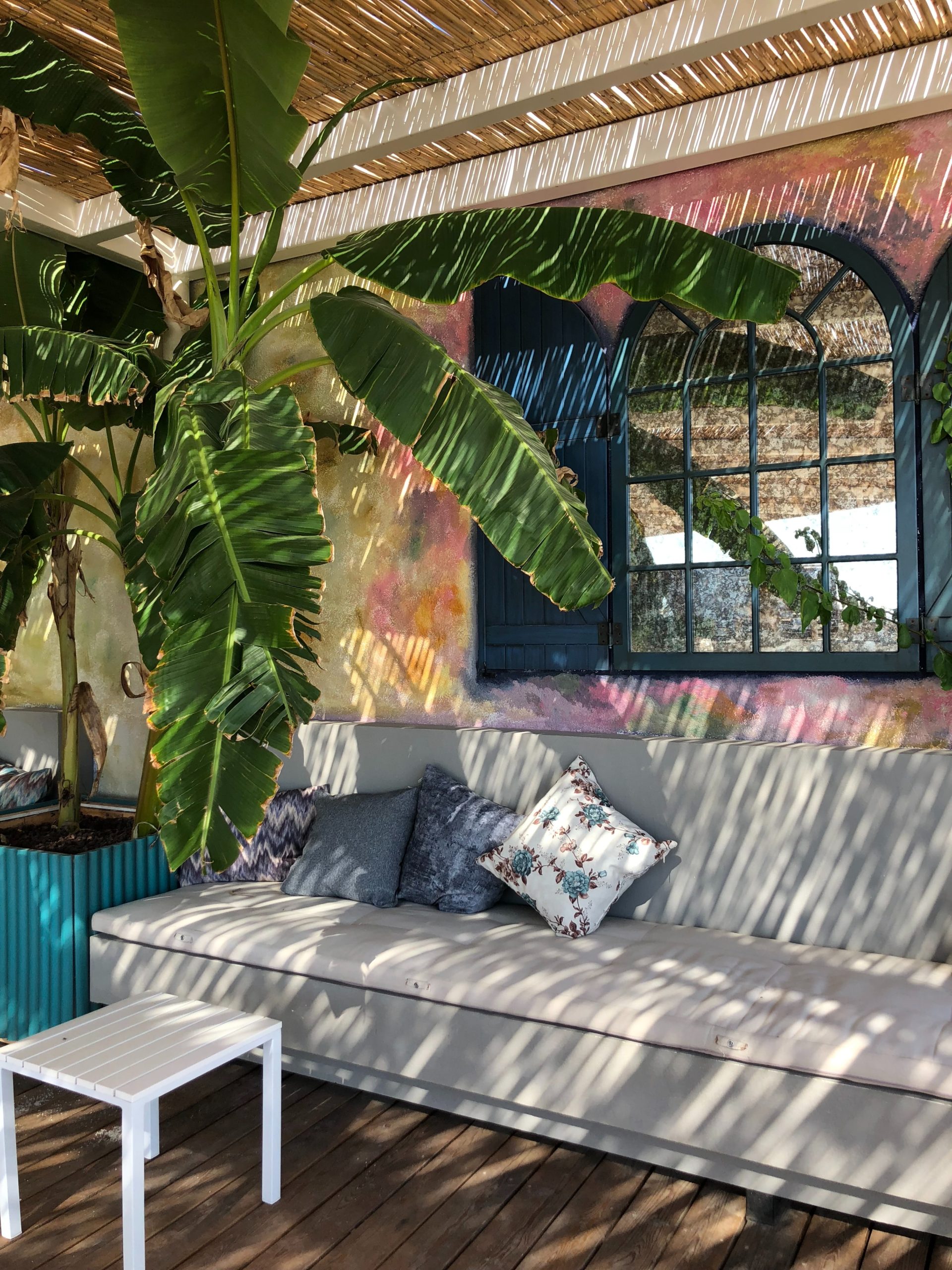 Terrasse ensoleillée décorée de plantes en pot, mobilier en rotin et voilage blanc, avec une pergola légère en bois pour filtrer la lumière, ambiance cosy et naturelle.