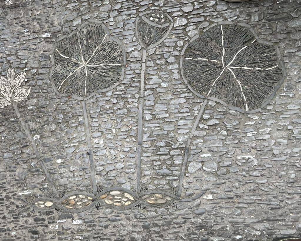 Dallage en galets et pierres représentant des feuilles et fleurs de lotus incrustées dans un mur, dans un style évoquant les traditions asiatiques.
