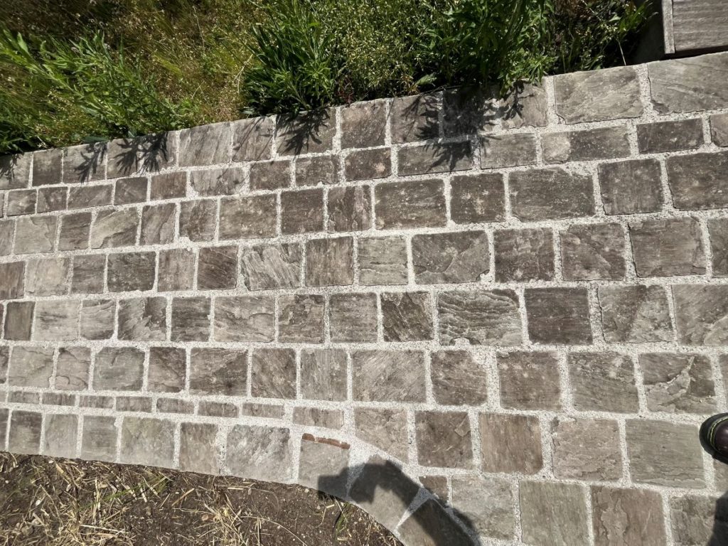 Allée ou terrasse réalisée en pavés de pierre réguliers de forme carrée et rectangulaire, posés en joint croisé avec joints clairs bien marqués.